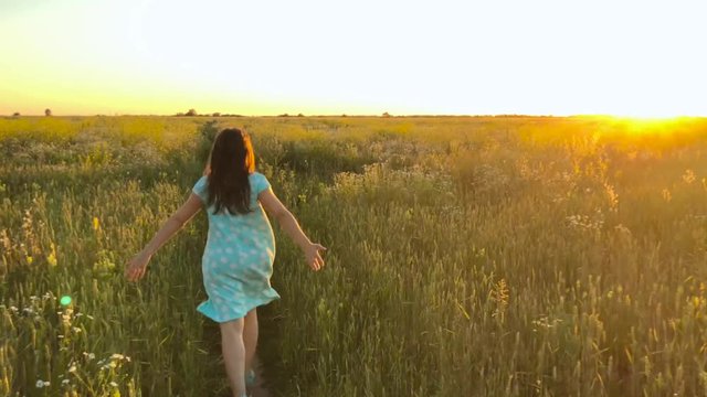 Beauty girl running on green wheat field over sunset sky. Freedom concept. Wheat field in sunset