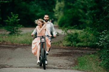 Catch me if you can sweetheart. The girl is riding a bicycle, and boyfriend running for her. Family on a walk in the forest. Couple in love. Love, romance, fun and healthy lifestyle concept.
