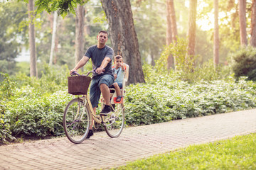 father and son riding a bicycle together outdoors in a city park.