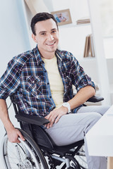 Home atmosphere. Cheerful young man keeping smile on his face, having pause