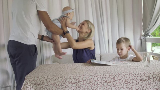Man give small baby daughter to a mother in cafe sitting at table with son