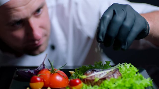 Chef is adding salt to the dish in slow motion. Chef is out of focus on the background