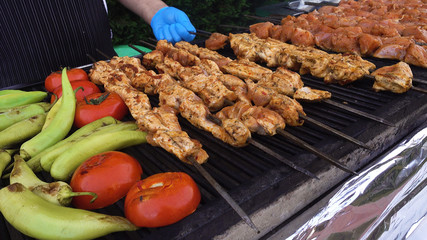 The chief is frying meat, peppers and tomatoes. Chicken meat with vegetables on the grill. Restaurant in the open air. The concept of a picnic, barbecue.