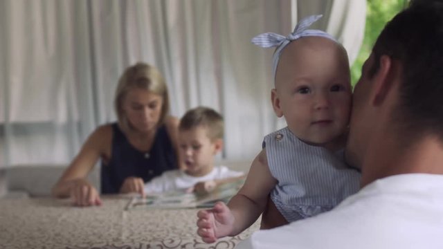 Little cute girl with bow on head looking at camera from father hands