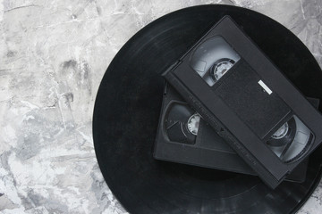 Retro vhs videocassettes from the 80s and vinyl records on a gray concrete background. The oldest...