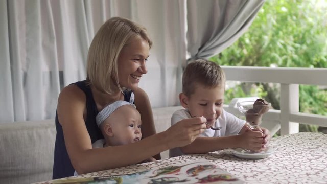 Mother feed her little son with ice cream in cafe