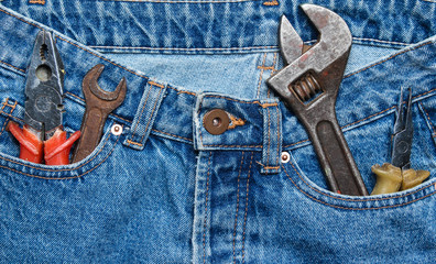 Work tool in the pocket of blue jeans. Pliers, wrench, adjustable wrench.
