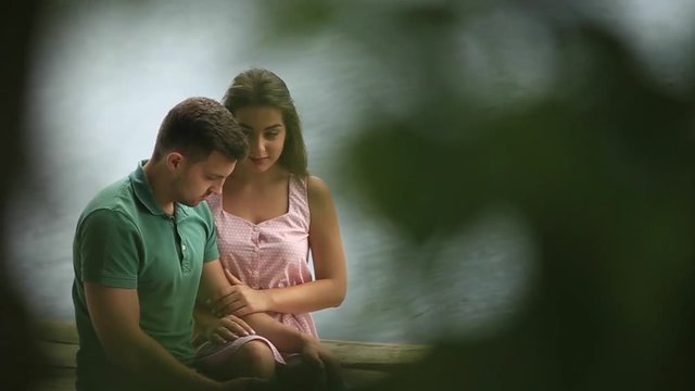 Beautiful youn couple sit on the pier near the lake. Close-up. 50fps