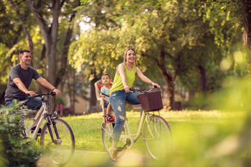 Smiling father and mother with kid on bicycles having fun in park..
