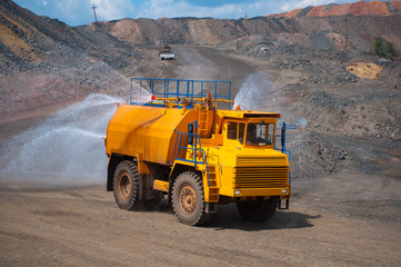 Obraz premium Heavy truck pours the road with water in the iron ore quarry. Dust removal, protection of the environment. Irrigation of the road from dust