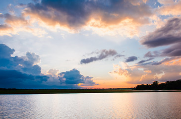 Sunset in the lake. Beautiful sunset behind the clouds above the over lake landscape background. Dramatic sky with cloud at sunset.