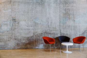 Concrete wall and white coffee table with red and navy chairs
