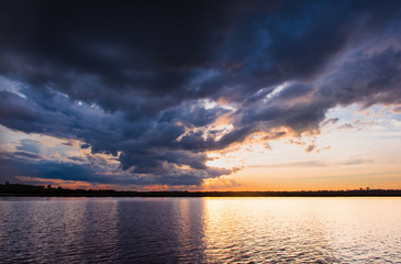 Sunset in the lake. Beautiful sunset behind the storm clouds before a thunder storm above the over lake landscape background. Dramatic sky with cloud at sunset.