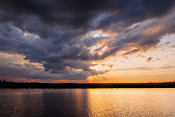 Sunset in the lake. Beautiful sunset behind the storm clouds before a thunder storm above the over lake landscape background. Dramatic sky with cloud at sunset.