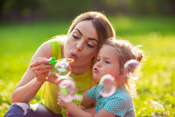 Female child blows soup foam and make bubbles with her mother in nature.