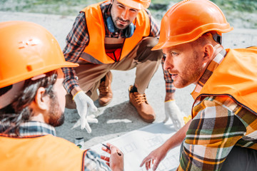 close-up shot of group of builders in hard hats having conversation about blueprint