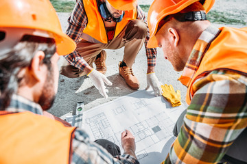 close-up shot of group of builders in hard hats having conversation about building plan