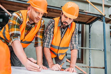 confident builders drawing building plan at construction site