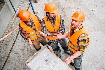 high angle view of group of confused builders discussing building plan at construction site