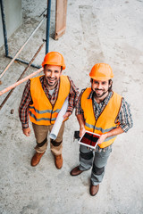 high angle view of builders with blueprint and tablet standing at construction site and looking at...