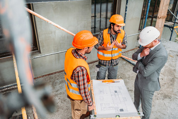 high angle view of confused builders and architect discussing building plan at construction site