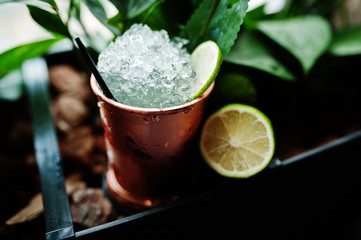 Alcoholic cocktail with ice and lime in bronze can glass on bar table.