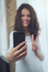 Portrait of careless pretty charming excited confident cheerful joyful cute lovely curly girl taking selfie with v-sign