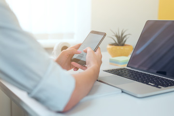 Close-up of female hands using modern smart phone while working at office with computer,...
