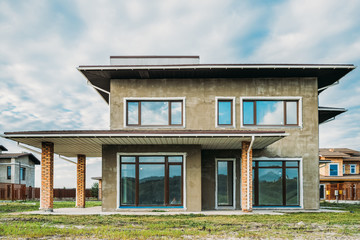 facade of unfinished modern concrete building with green yard under cloudy sky