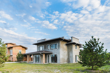 unfinished contemporary buildings with green yards on cloudy day with fir trees on foreground