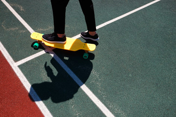Close up photo of modern man in stylish wear keeping feet on yellow skateboard