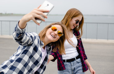 Two young happy girl friends in hipster making selfie on phone
