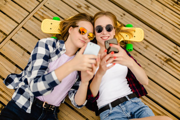 Two young girl in hipster outfit making selfie while lying with on wooden pier
