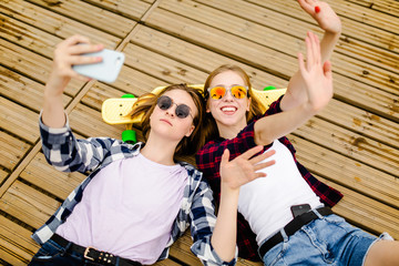 Two young girl in hipster outfit making selfie while lying with on wooden pier