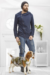 Full length portrait of a young handsome man with dressed Beagle in the white room. The hipster guy...