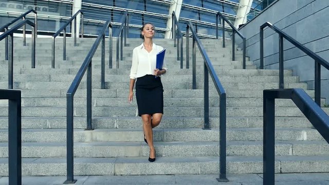 Business Woman In Skirt And Blouse, Holding Foulder And Walking Down Stairs. Slow Motion.