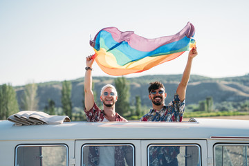 Smiling couple in van holding rainbow flag