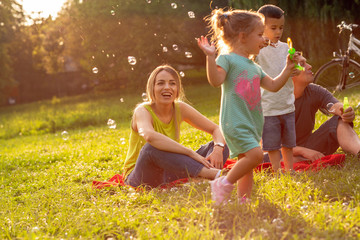 family, parenthood, adoption and people concept – Happy family with children blow soap bubbles in...