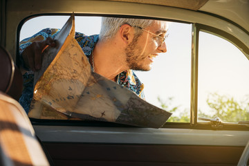 Cheerful man with map looking outside a car