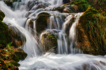Fototapeta na wymiar Small waterfall, water stream between rocks and grass