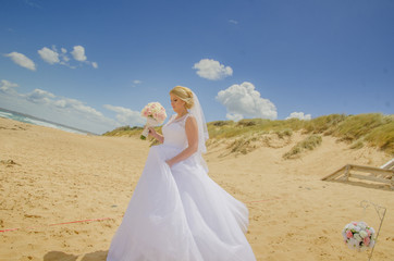 Fototapeta na wymiar Beautiful bride wearing white wedding dress with bouquet in her hands at beach. Shot at wedding in Australia on amazing sand beach.