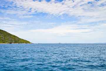 coastline of the island, sea horizon, small fishing boats off the island, against the blue sky and clouds