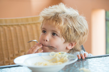 Child eats spaghetti with a fork. Food for children. Italian pasta for a small child. Healthy food, lunch in the garden. Handsome boy does not want to eat. Baby food