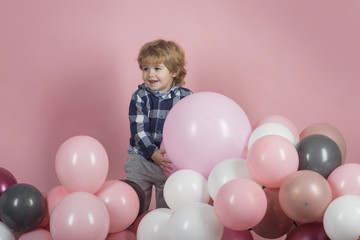 Fototapeta na wymiar Happy child with balloons. Boy with toys on a pink background. No sexism. A boy in a blue shirt on a pink background. Attractive little man is playing in the garden. Happy childhood