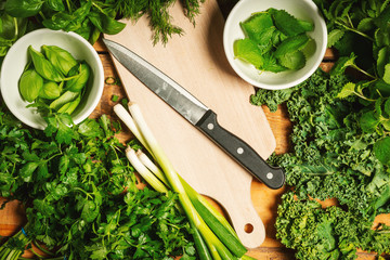 background with green vegetables and spices on a wooden table with a knife