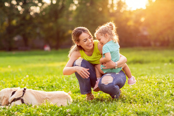 Fototapeta premium happy family is having fun with golden retriever - Mother and her daughter playing with dog in park.