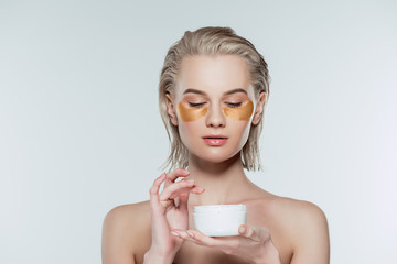 woman with eye patches and face cream in plastic container, isolated on grey