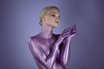 tender stylish girl painted with ultra violet glitter, isolated on purple