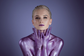attractive fashionable woman painted with purple glitter, isolated on violet