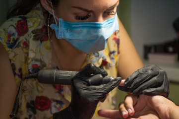 The master of nail extensions makes the hardware and trimmed manicure to his client in the beauty...